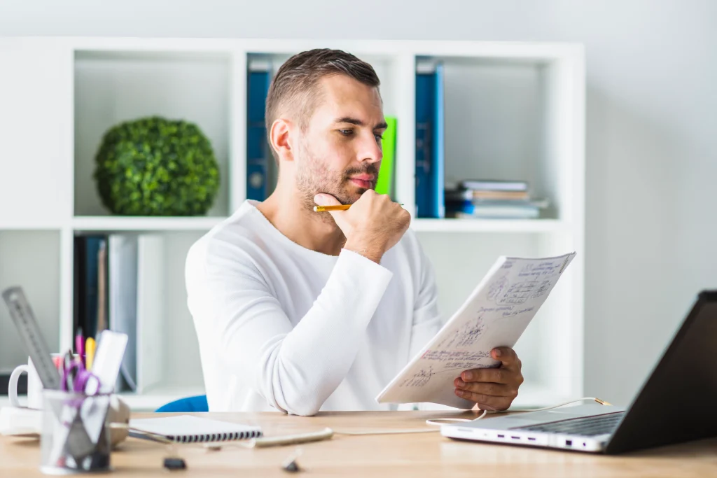 Man reviewing notes at his desk with a laptop