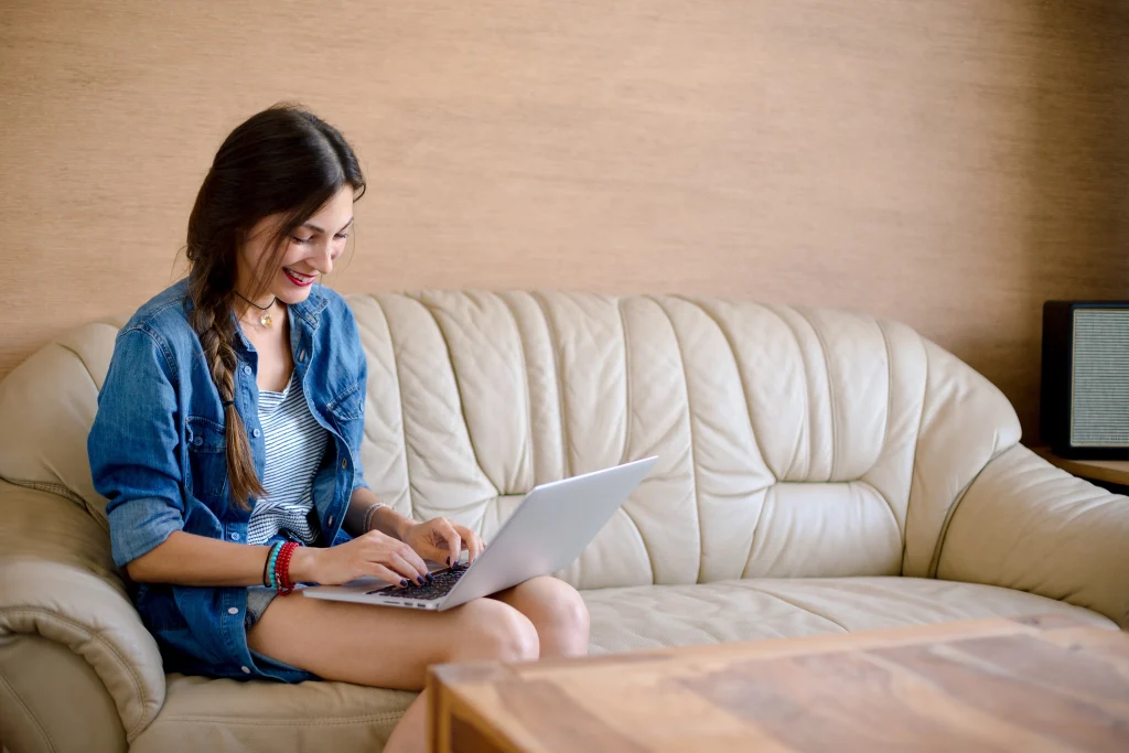 A woman using a laptop on a beige sofa. The setting is cozy and casual, creating a relaxed atmosphere.